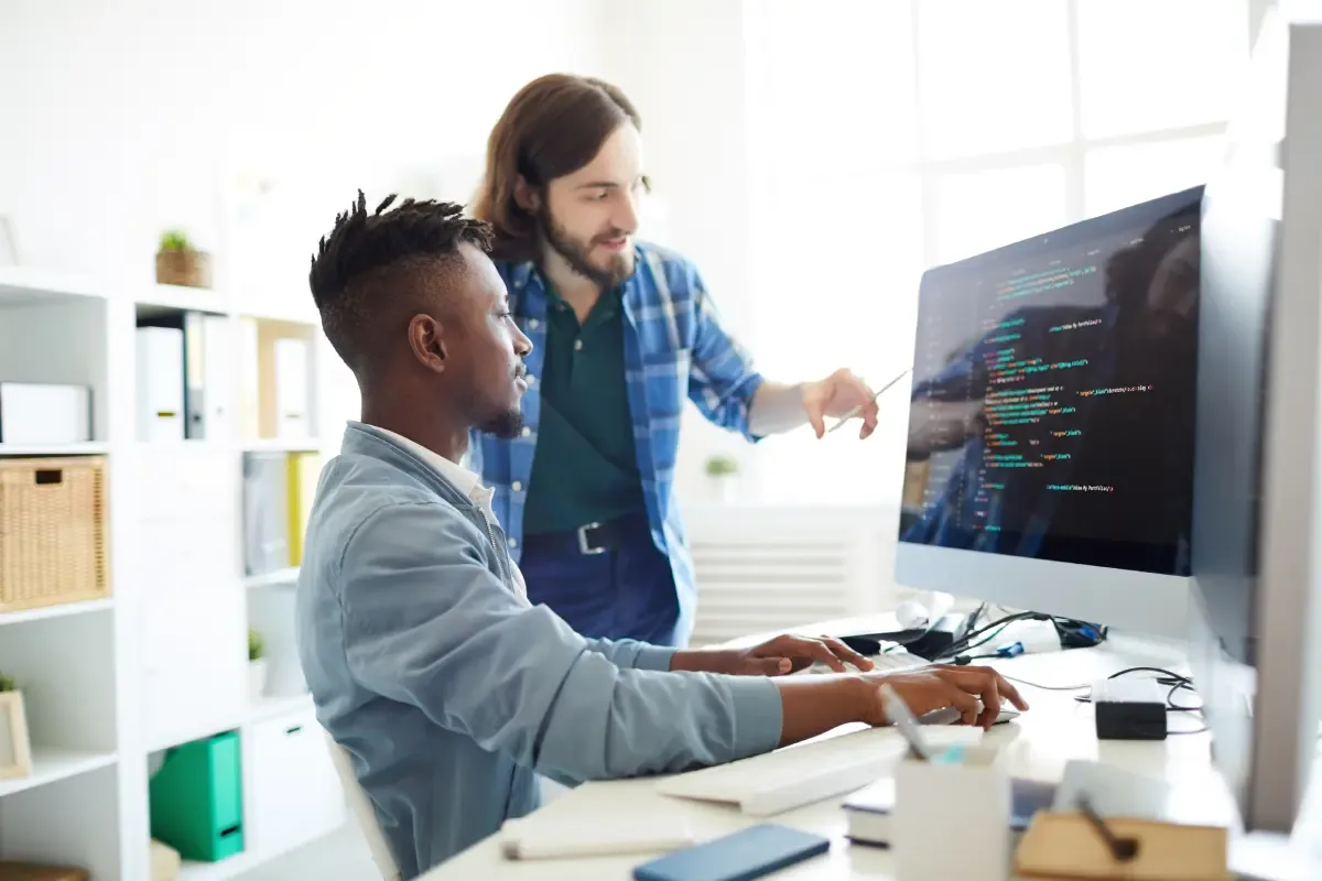 Two software developers discussing code at a workstation